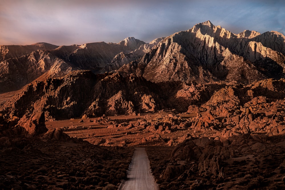 a dirt road surrounded by mountains under a cloudy sky