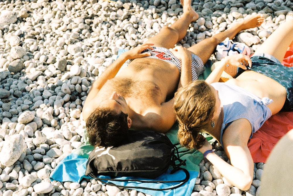 a man and a woman laying on a rocky beach