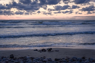 A serene beach with gentle waves lapping against smooth stones at dusk.
