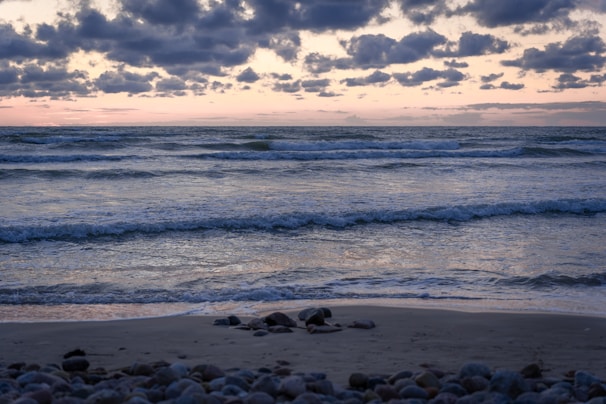 A serene beach with gentle waves lapping against smooth stones at dusk.