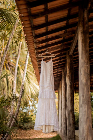 Vibrant orange tropical dress hanging on a rustic wooden hanger with a backdrop of lush green leaves