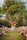 A couple stands at the altar under a large tree adorned with string lights, creating an intimate outdoor wedding atmosphere. The surrounding area is decorated with colorful floral arrangements and guests are seated along the aisle.