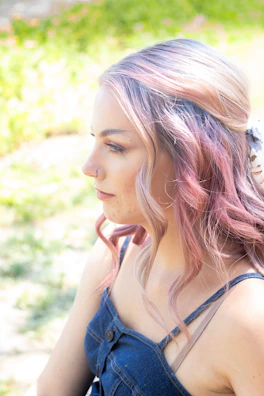 A young woman with lavender ombre hair styled in loose waves, smiling outdoors.