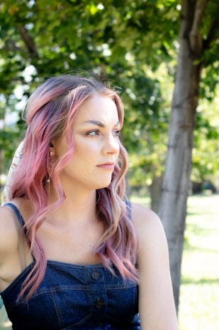 A woman wearing a soft pink top in a sunny park.