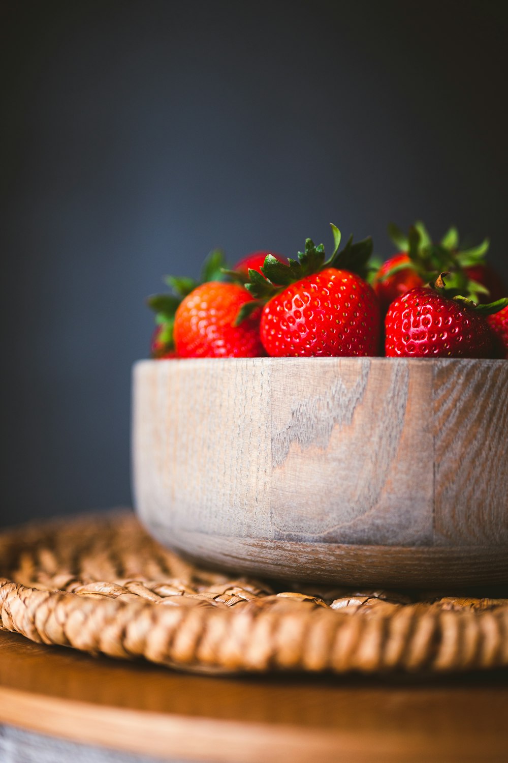 a wooden bowl filled with strawberries on top of a table