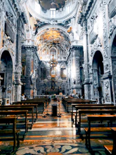 Interior shot of the Basilica di Sant'Anastasia al Palatino showing ornate frescoes and wooden pews bathed in soft light.