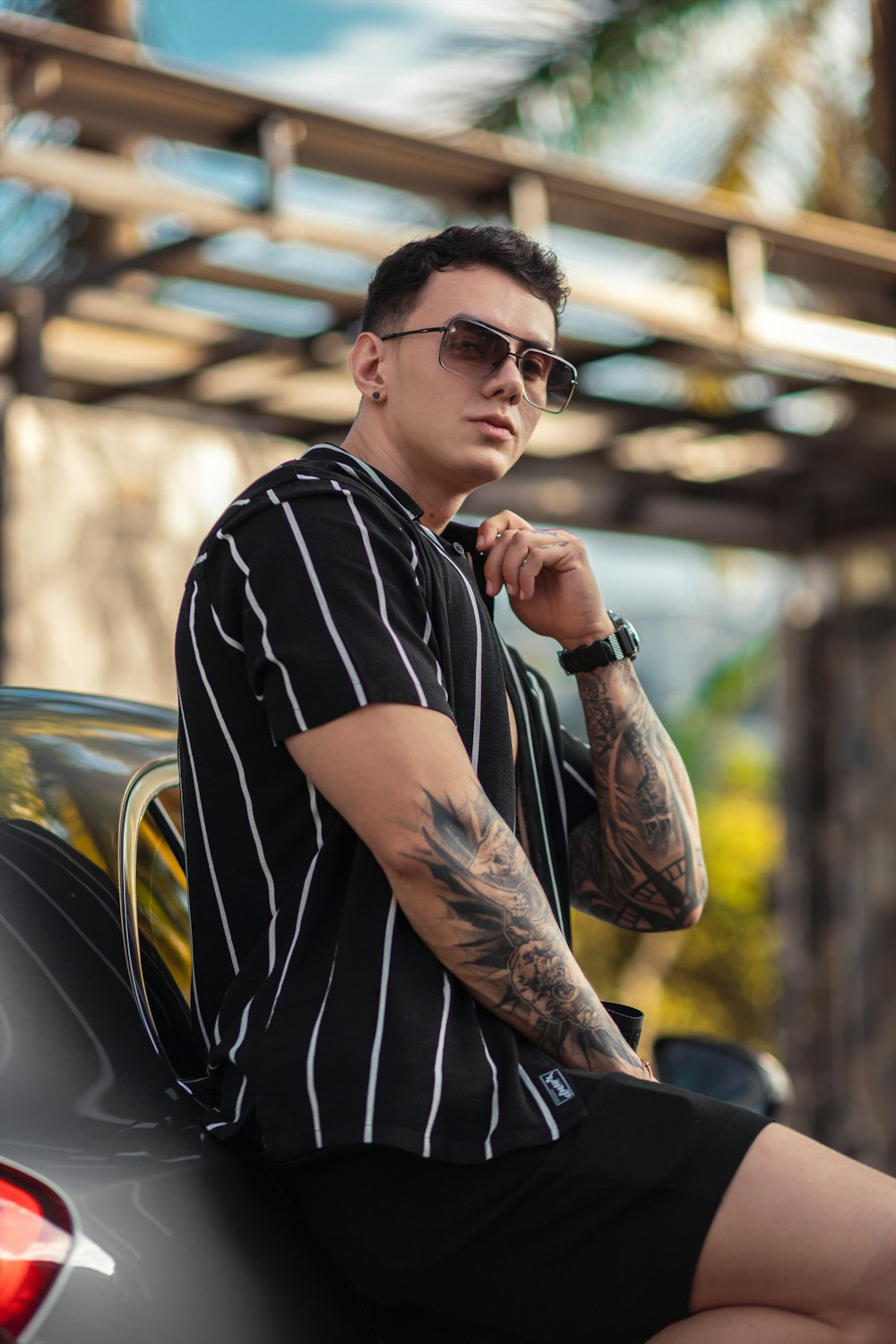 a man with tattoos sitting on the hood of a car