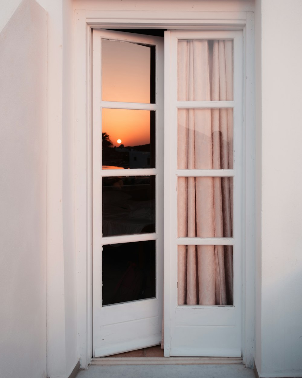 a window with a curtain and a sunset in the background