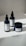 Three hemp-based skincare products are arranged on a smooth, white surface. Two are dropper bottles with dark blue glass and white labels, and one is a small jar with a screw-top lid, also featuring a white label. Natural lighting casts soft shadows on the surface.