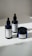 Three hemp-based skincare products are arranged on a smooth, white surface. Two are dropper bottles with dark blue glass and white labels, and one is a small jar with a screw-top lid, also featuring a white label. Natural lighting casts soft shadows on the surface.
