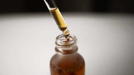 Amber essential oil drops falling from a glass bottle beside nutmeg pods.