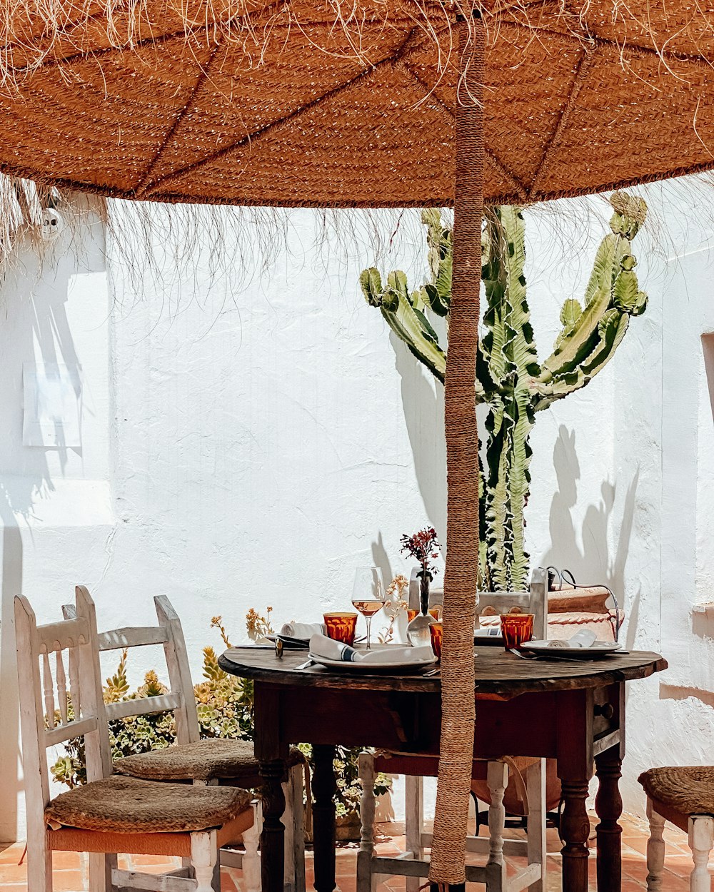 a table and chairs under an umbrella with a cactus in the background