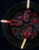 A colorful assortment of berry popsicles arranged on a rustic wooden board.