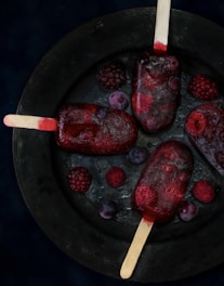 Vibrant red and blue berry popsicles arranged on a rustic wooden board with fresh berries scattered around.
