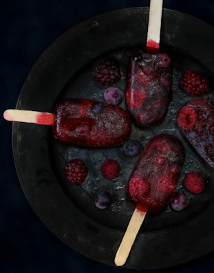 A colorful assortment of berry popsicles arranged on a rustic wooden board.
