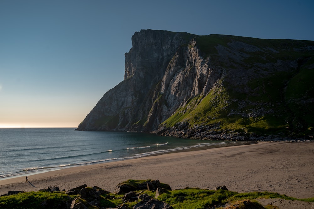 a sandy beach next to the ocean with a mountain in the background