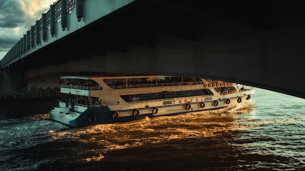 a large white boat traveling under a bridge