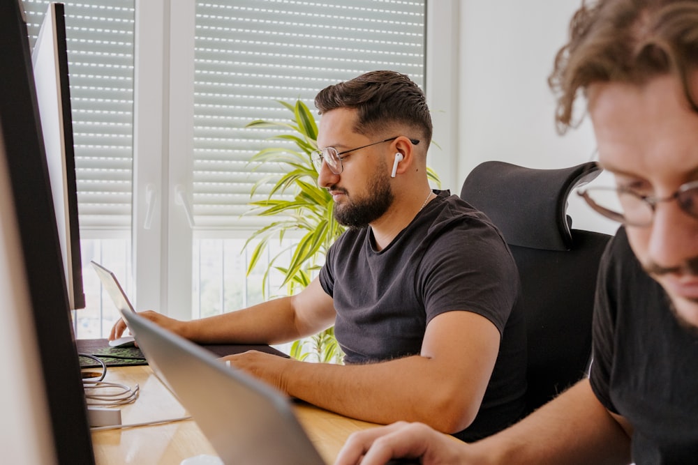 two men sitting at a desk looking at a laptop