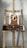A wooden easel displays a painting of a dog with a brown and white fur. The background is a splattered paint wall with various colors. The easel is equipped with a tray holding various paint smudges.