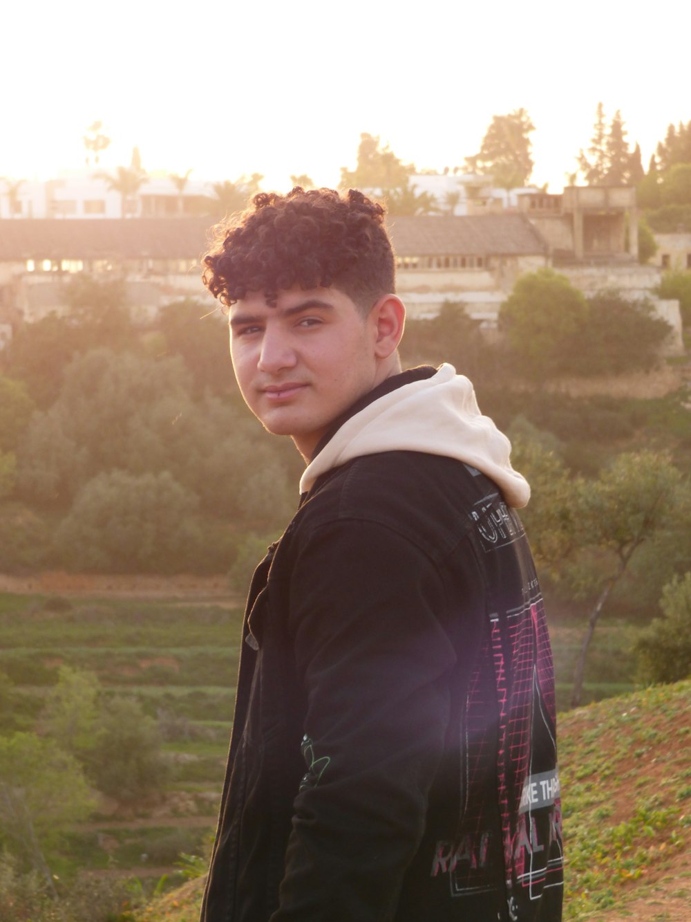 a young man standing in front of a lush green hillside