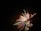 Vibrant fireworks burst against the night sky, displaying an array of colors including green, red, yellow, and blue. The streaks of light fan outwards, creating a dynamic and festive pattern.