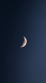 A delicate silver crescent moon cradling a cluster of twinkling stars against a deep midnight blue cosmic background.