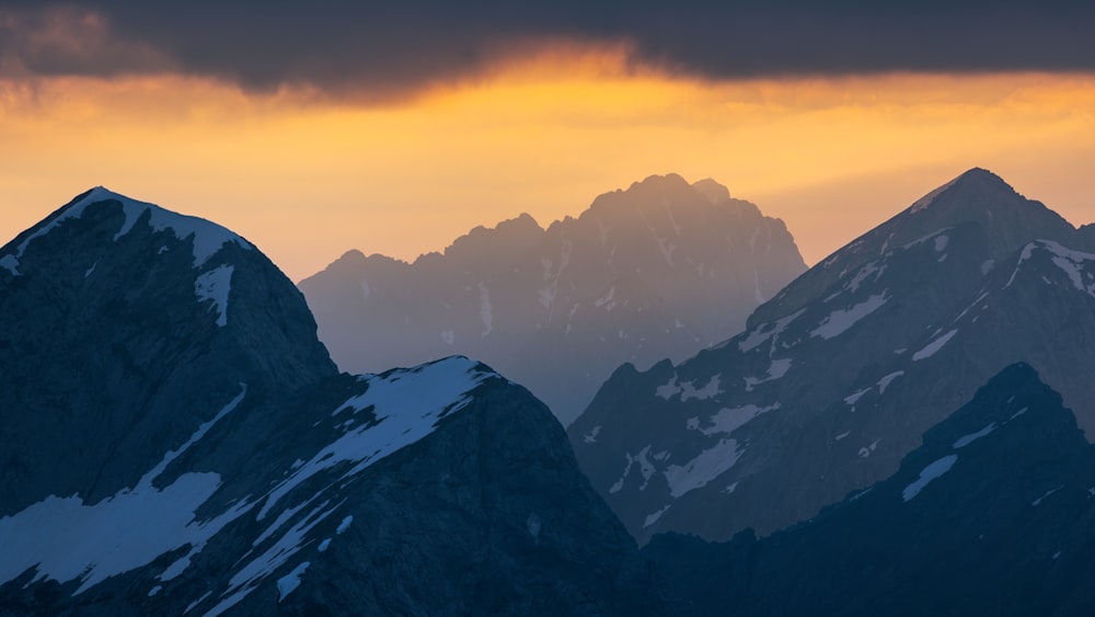 a group of mountains covered in snow under a cloudy sky