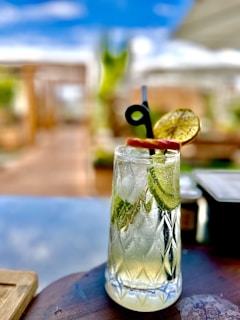 A chilled glass of traditional tejuino with condensation, garnished with lime and served with a straw on a sunny outdoor café table.