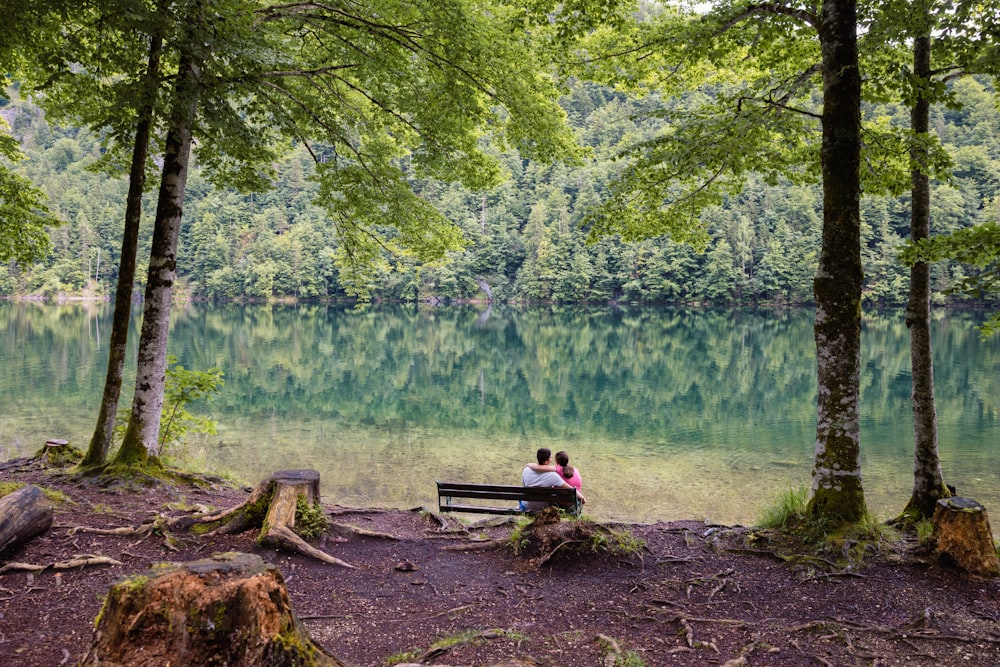 two people sitting on a bench in front of a lake