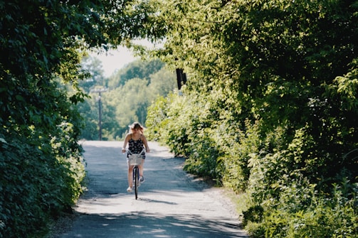 A candid photo of a person riding a bicycle in a sunny park, surrounded by greenery.