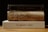 A stack of three books is placed on a wooden surface. The top book is titled 'HOLY BIBLE' with a dark cover. The middle book appears old and worn, with noticeable damage and frayed edges. The bottom book has a clean beige cover and is titled 'THE KINGDOM'S JOURNEY'.