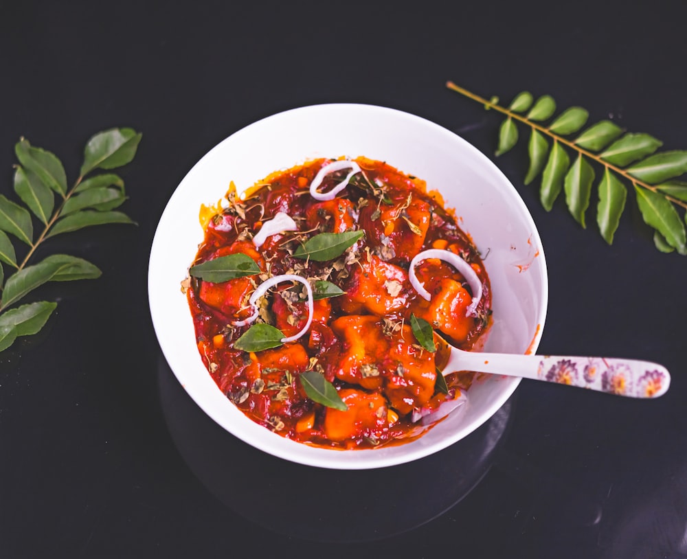 a white bowl filled with stew next to a leafy branch