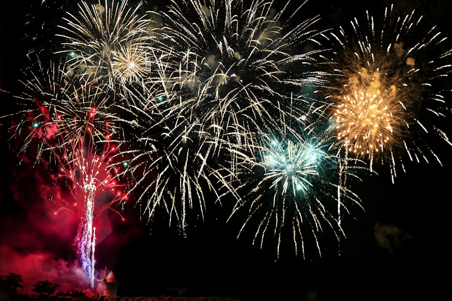 A vibrant display of fireworks lighting up the night sky with bursts of gold, red, and blue. The colorful explosions create a dazzling spectacle with intricate patterns and trails of light.