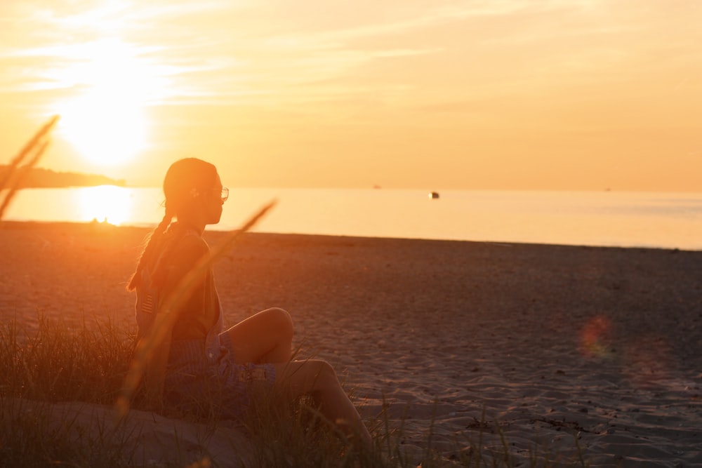 a woman sitting on the beach watching the sun go down