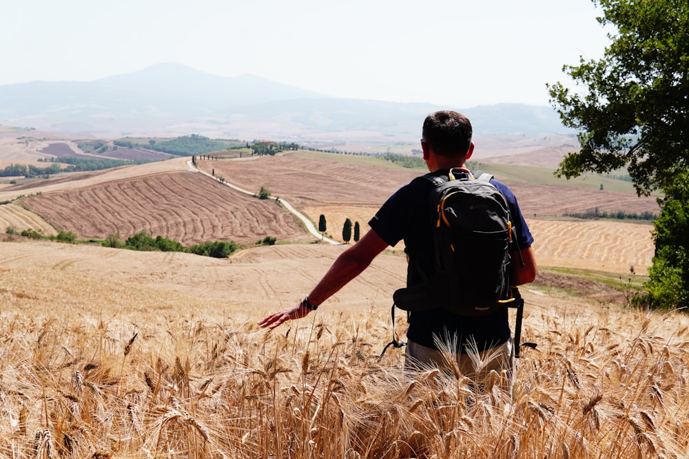 a man with a backpack walking through a wheat field