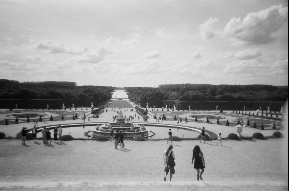a black and white photo of people walking around a fountain