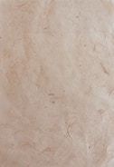 A textured paper surface with a natural, slightly rugged appearance featuring subtle lines and small spots. The paper has a light brown, almost beige hue with visible fibers embedded within the material.