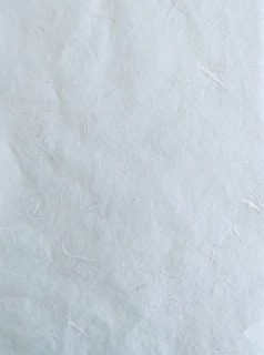 A textured surface with subtle creases and wrinkles, resembling handmade paper. The surface is primarily uniform in color with slight imperfections and variations.
