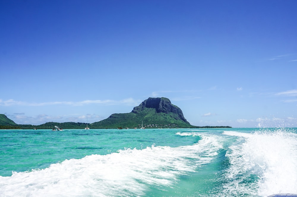 the wake of a boat in the ocean with a mountain in the background