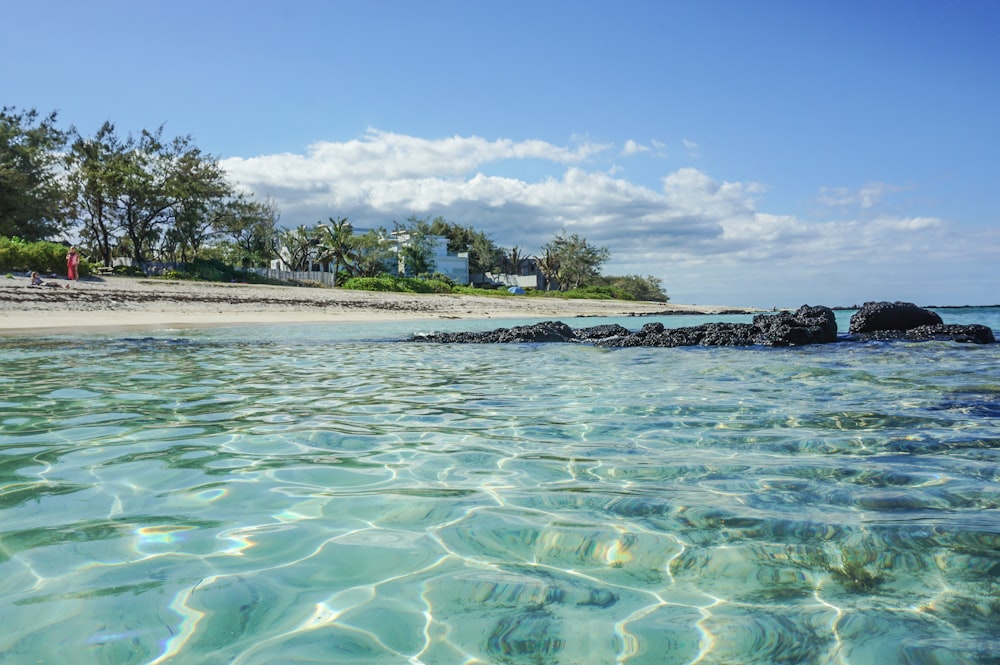 a beach with clear blue water and a white house in the distance