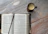 Close-up of a steaming coffee mug beside a bookmark resting on a textured wooden table.
