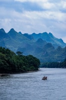 Wide shot of a raft floating down a calm stretch of river surrounded by lush greenery.