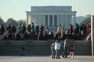 A lively group of people gathered around a historic landmark during a sunny outing.