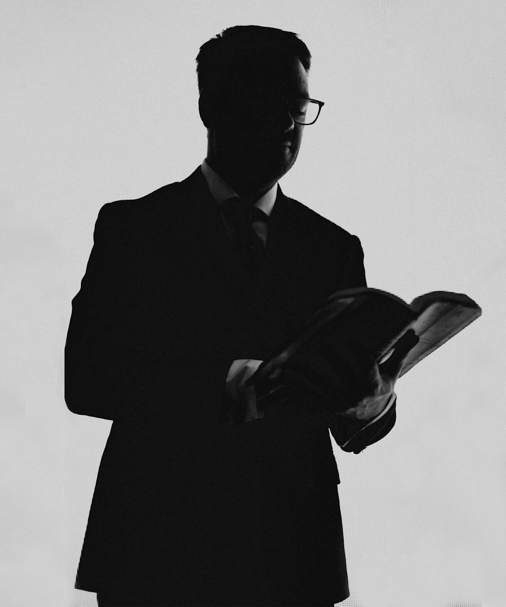 a black and white photo of a man in a suit reading a book