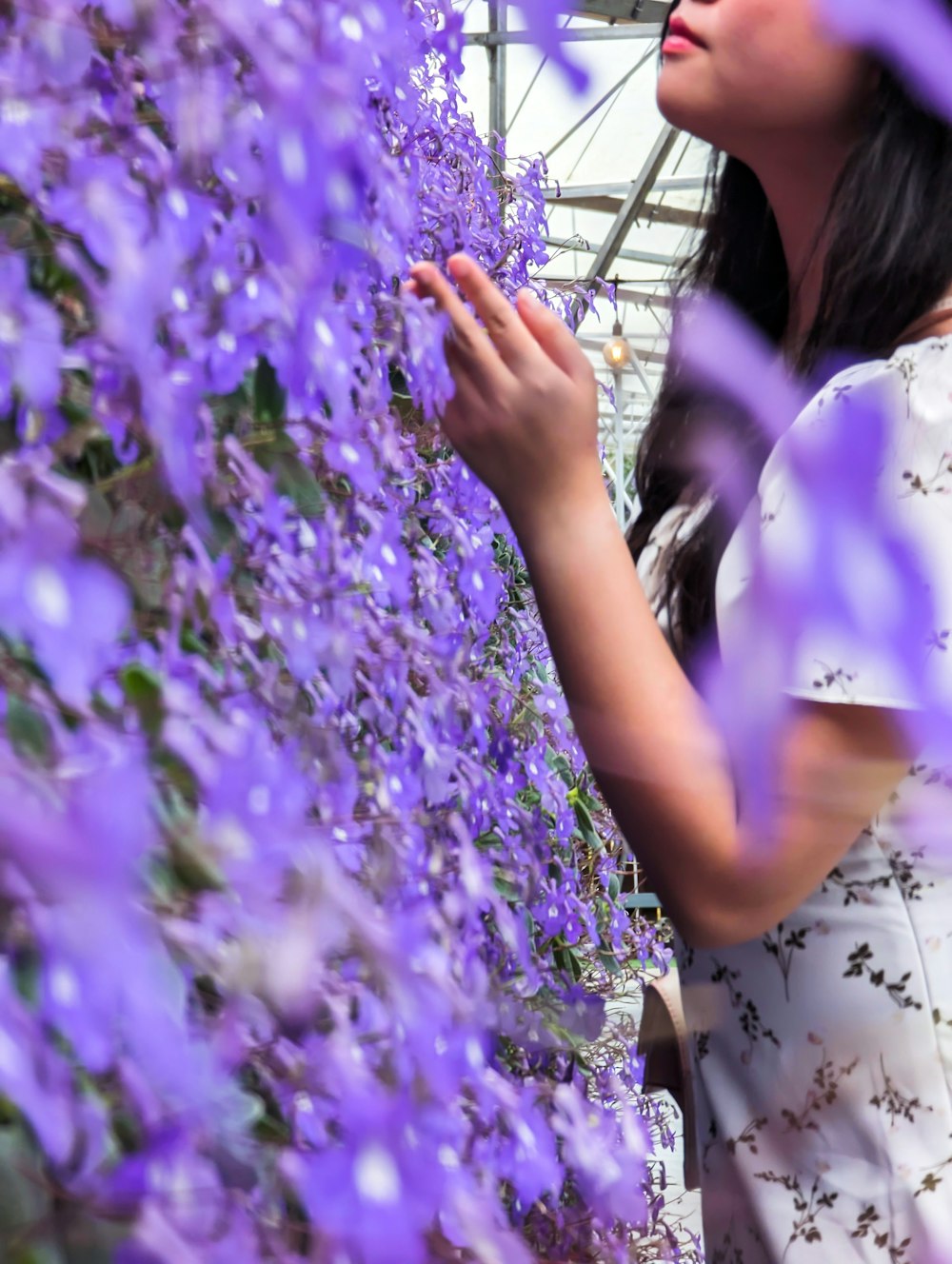 a woman looking at purple flowers in a greenhouse