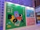 A vibrant advertisement board for the Hong Kong Book Fair 2023 is displayed. The board features colorful graphics including books, a ruler, and playful designs with large letters spelling 'BOOK FAIR'. The layout includes information about different exhibition halls and the World of Snacks event. The colors range from green, blue, to pink, creating an engaging atmosphere.