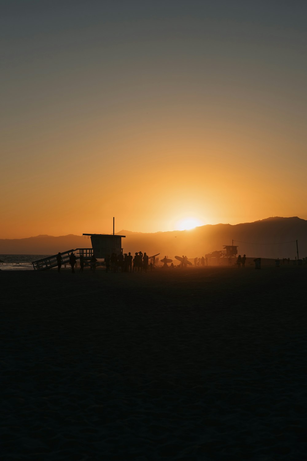 the sun is setting over a beach with a lifeguard tower