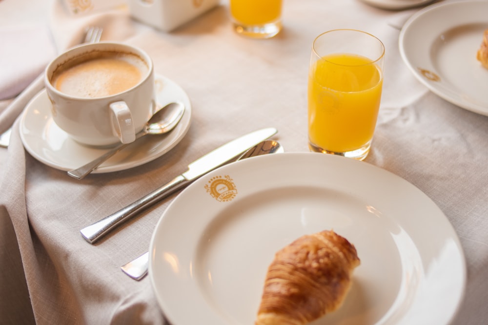 a plate with a croissant on it next to a cup of coffee