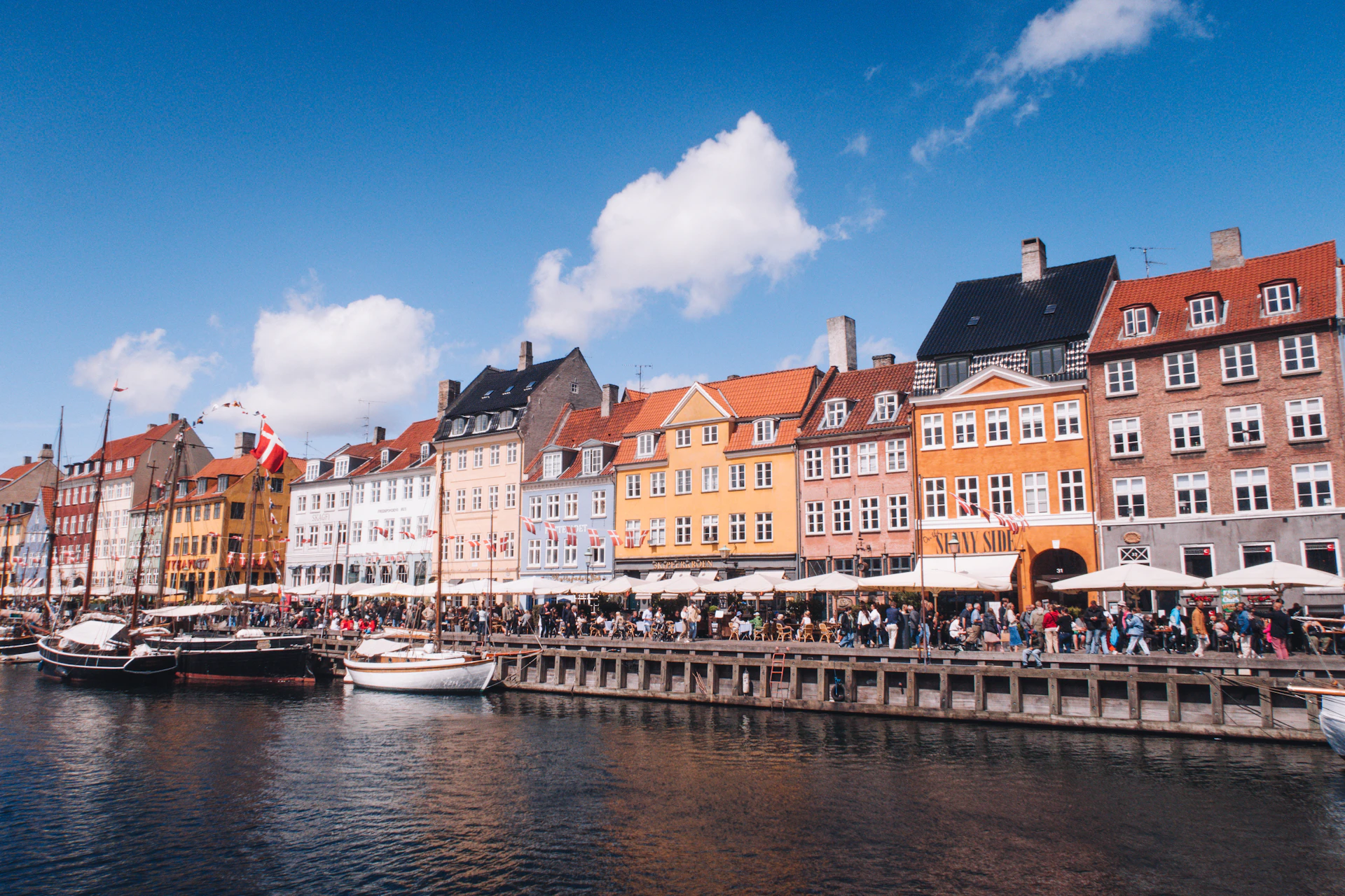 a group of people walking along a river next to buildings