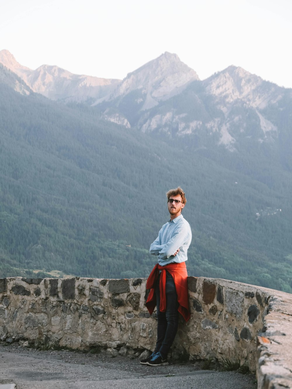 a man leaning on a stone wall with mountains in the background